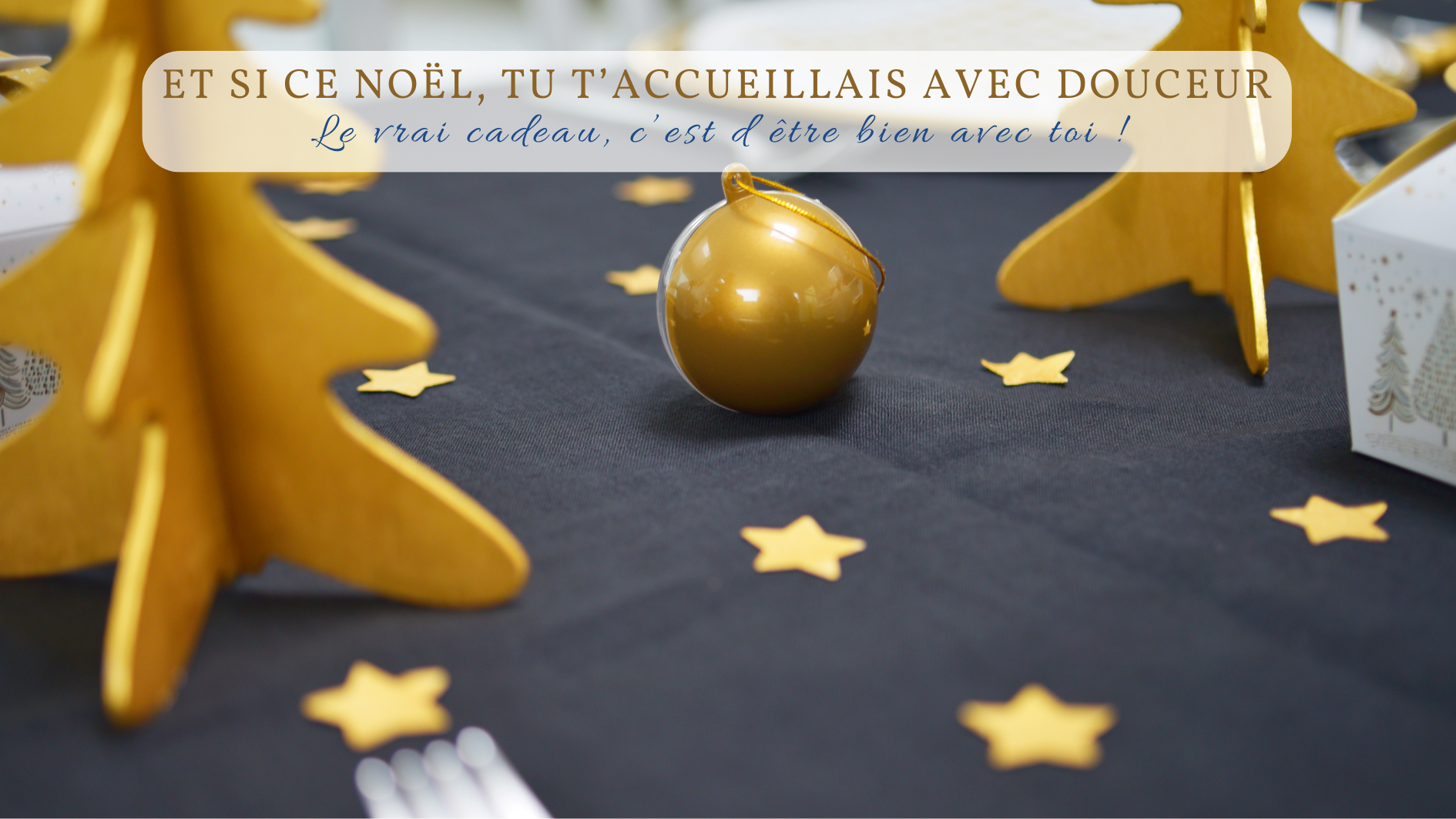 Pour le temps des fêtes, une table de Noël décorée sobrement avec des étoiles dorées, des sapins en bois jaune et une boule festive, évoquant une ambiance chaleureuse et douce.